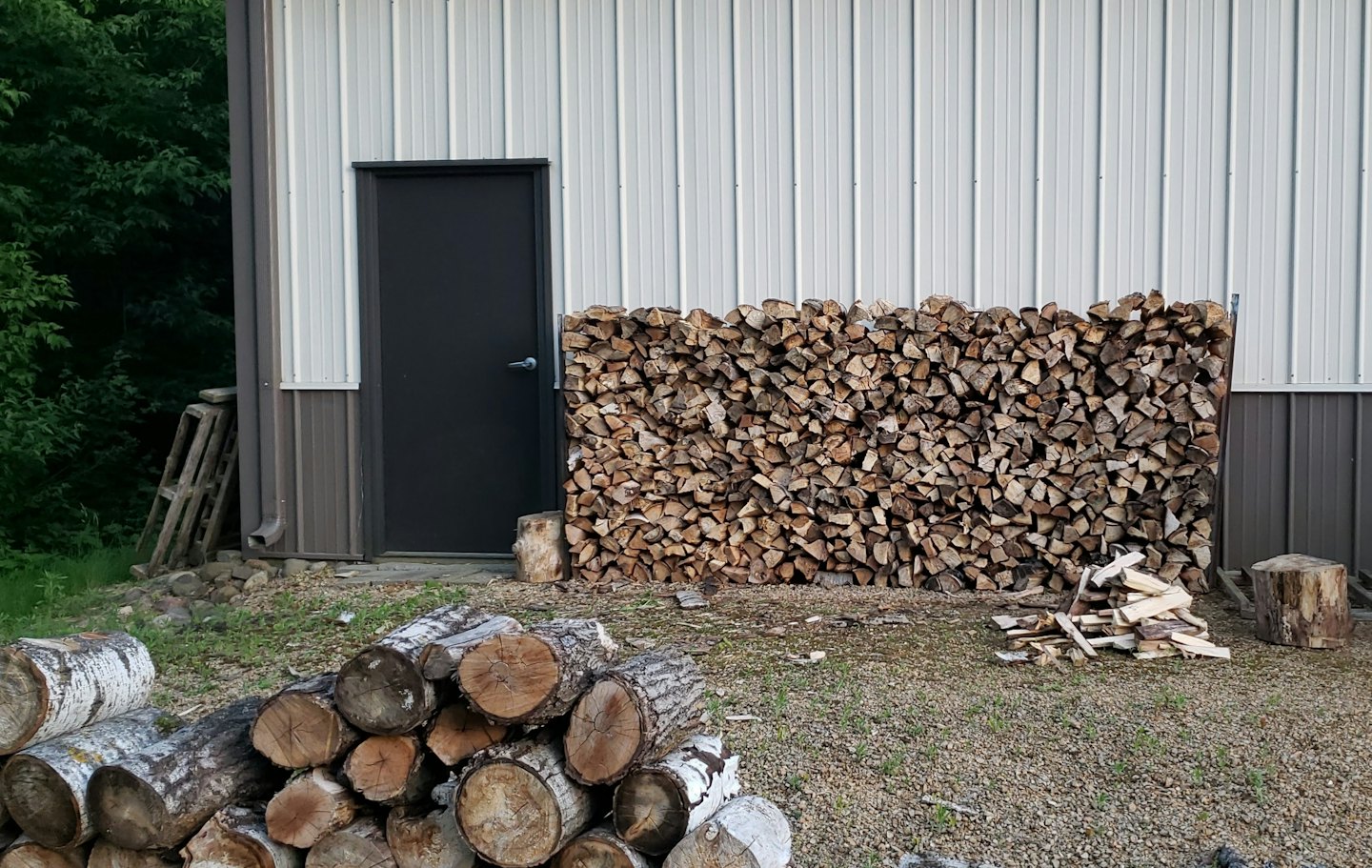 Laotud küttepuud metallist abihoone seina ääres.